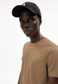 Bruine katoenen t-shirt met ronde hals, gecombineerd met een zwarte pet met een wit logo. Eenvoudige textuur en snug fit ontwerp.