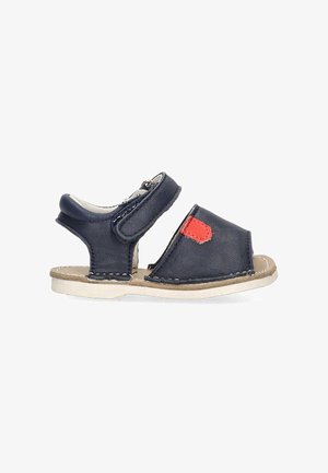 Sandal de cuero azul con una correa de velcro, diseño de punta abierta, suela beige y un parche de acento rojo, con detalles de costura.