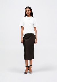 White cotton t-shirt with short sleeves and front print, paired with a dark brown satin midi skirt and black high-heeled sandals.