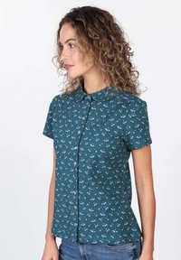 Short-sleeve button-up shirt in teal with a floral pattern, featuring a collared neckline and soft, textured fabric.