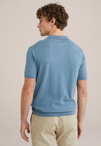 Camisa polo de manga corta de color azul claro. Cuello y dobladillo acanalados. Textura suave con un sutil patrón de punto. Llevada con pantalones beige texturizados.