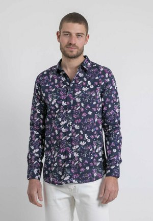 Chemise à fleurs avec un fond bleu marine foncé, ornée de motifs colorés de fleurs roses, blanches et vertes. Conception à manches longues et col boutonné.