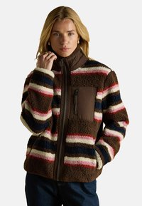 Braune Fleecejacke mit buntem Streifenmuster in Blau, Rot und Creme. Mit hohem Kragen und Reißverschlusstasche auf der Brust. Weicher Stoff.