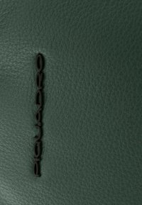 Superficie de cuero verde con un acabado texturizado; presenta un logotipo negro prominente "Piquadro" en relieve, colocado verticalmente sobre el material.