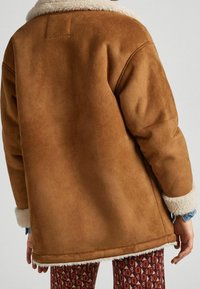 Mörkbrun fuskpälsjacka med mjuk textur, krämfärgad fluffig krage och manschetter, med en lös passform och stickade sömdetaljer.