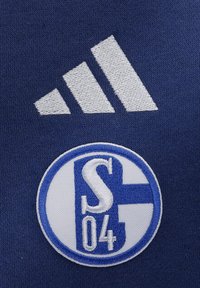 Il tessuto di cotone blu navy presenta un logo Adidas bianco e un'emblema circolare ricamato con accenti blu e il testo "S 04" al centro.