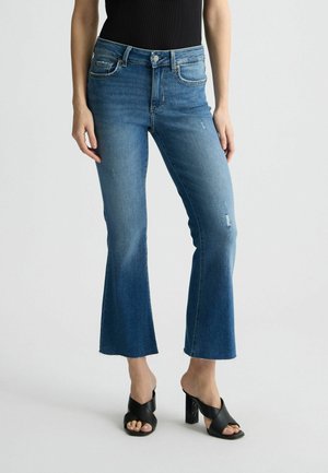 Jeans a vita alta blu a gamba larga con dettagli strappati e orlo grezzo. Abbinati a mules neri con tacco a blocco decorato.