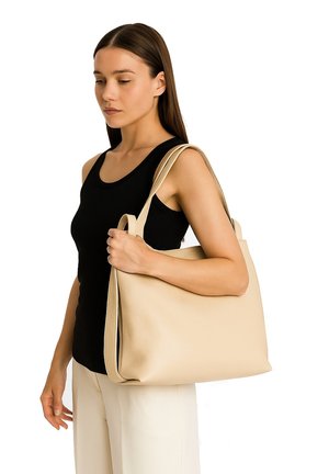 Borsa tote in pelle beige con texture liscia, doppi manici e un design spazioso, indossata a spalla da una persona in una maglietta nera.
