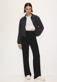 Čierne nohavice s vysokým pásom v kombinácii s krátkym sivým topom a čiernou bomber bundou; disponujú voľným strihom a minimalistickým dizajnom.