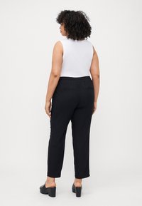 Pantaloni neri con vita elasticizzata, tasche inclinate, vestibilità larga e gambe dritte abbinati a un top bianco senza maniche e sandali neri con plateau.