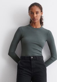 Zeleni dugi rukav, pripijen top s okruglim izrezom, izrađen od rebraste tkanine, u kombinaciji s crnim trapericama visokog struka. Jednostavan i elegantan dizajn.