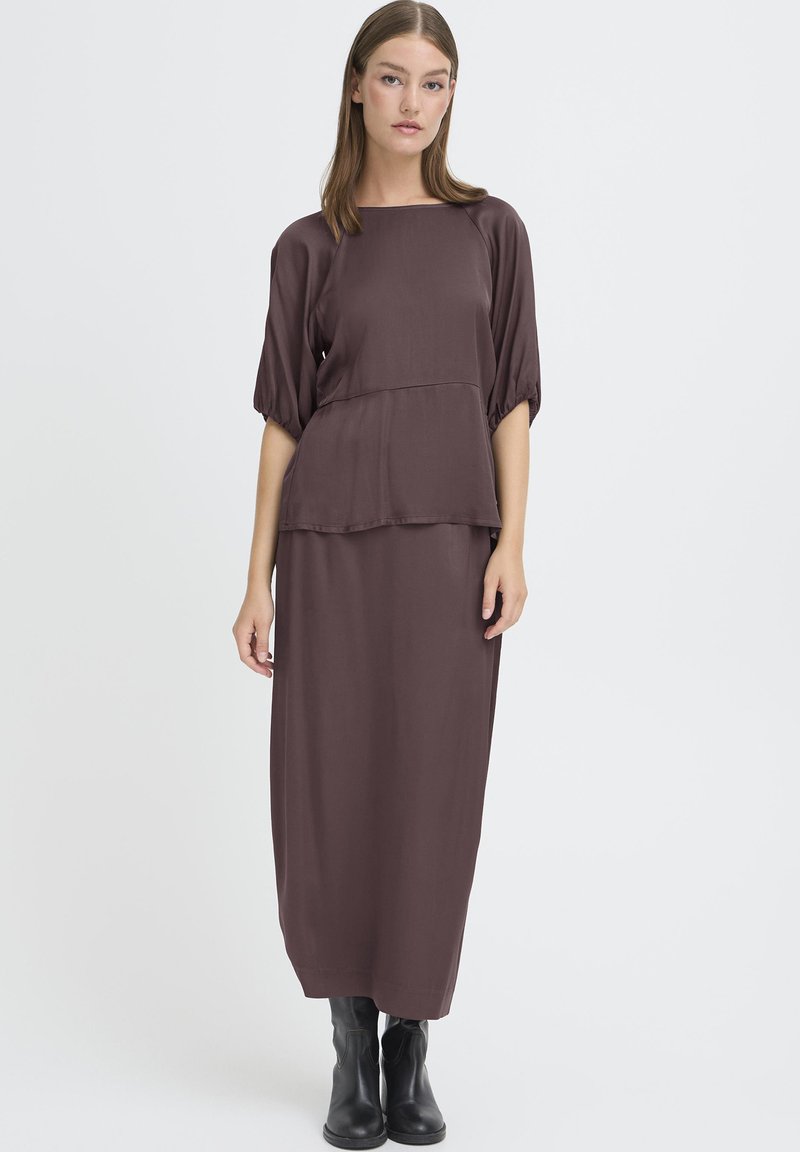 Brun, langærmet, knælang kjole med en afslappet pasform og lagdelt peplum-design, lavet af glat stof. iført sammen med sorte ankelstøvler.