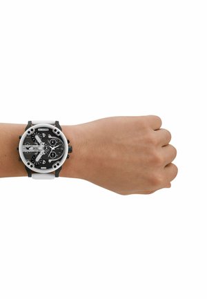 Orologio Diesel in bianco e nero indossato su una mano, con una cassa rotonda, diversi quadranti e un cinturino in gomma testurizzata. Segni sul quadrante.