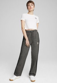 Sort og grå ternede bukser med snøre i taljen og sorte striber på siderne; sættet er kombineret med en hvid cropped t-shirt med et logo.