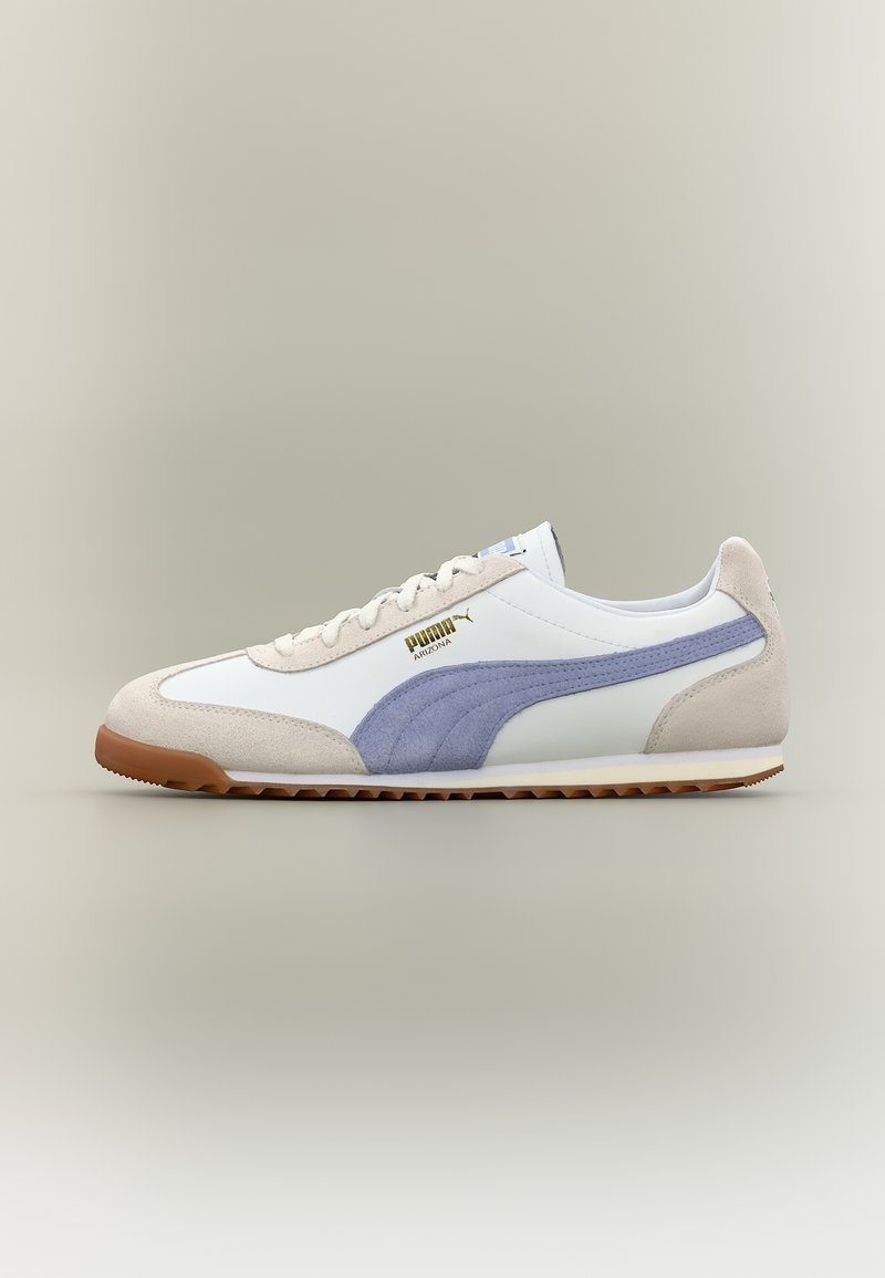 Λευκό και μπεζ αθλητικό παπούτσι Puma Arizona με μπλε ρίγα και καφέ σόλα, που φαίνεται από το πλάι σε ουδέτερο φόντο.