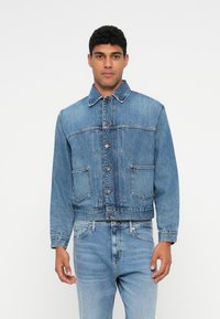 Τζιν μπουφάν σε ανοιχτό γαλάζιο με γιακά, κουμπιά μπροστά και δύο τσέπες στο στήθος. Διαθέτει κομψή, κοντή εφαρμογή και διακριτική υφή. Συνδυάζεται με ανοιχτό γαλάζιο τζιν παντελόνι.