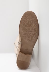 Botte en daim beige avec une semelle en caoutchouc texturée, présentant un motif floral et un détail de fermeture éclair latérale. Marquage de la taille visible sur la semelle.