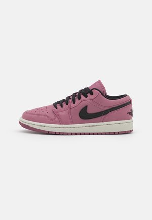 Niski sneaker z kulistej różowej skóry z czarnymi sznurowadłami, czarnym logo Nike, białą podeszwą środkową i różową zewnętrzną na jednolitym tle.