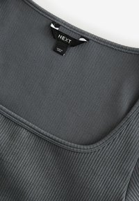 Débardeur gris à côtes avec un col large. Le tissu a une texture lisse et présente une étiquette de marque portant l'inscription "NEXT."