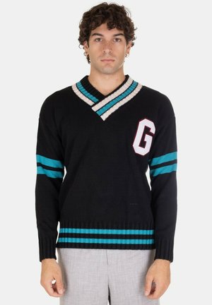 Maglione nero a maglia con scollatura a V, caratterizzato da accenti a strisce turchesi e bianche, e una patch rossa con la lettera "G" sul petto. Maniche e orlo a costine.