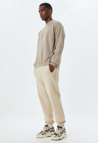 Sudadera beige con puños acanalados, combinada con joggers beige suaves con bolsillos laterales, completada con zapatillas beige y negras con un patrón.