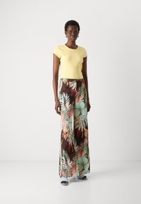 Yellow fitted t-shirt paired with wide-leg trousers featuring a brown background and colorful floral patterns. Soft texture and modern fit.