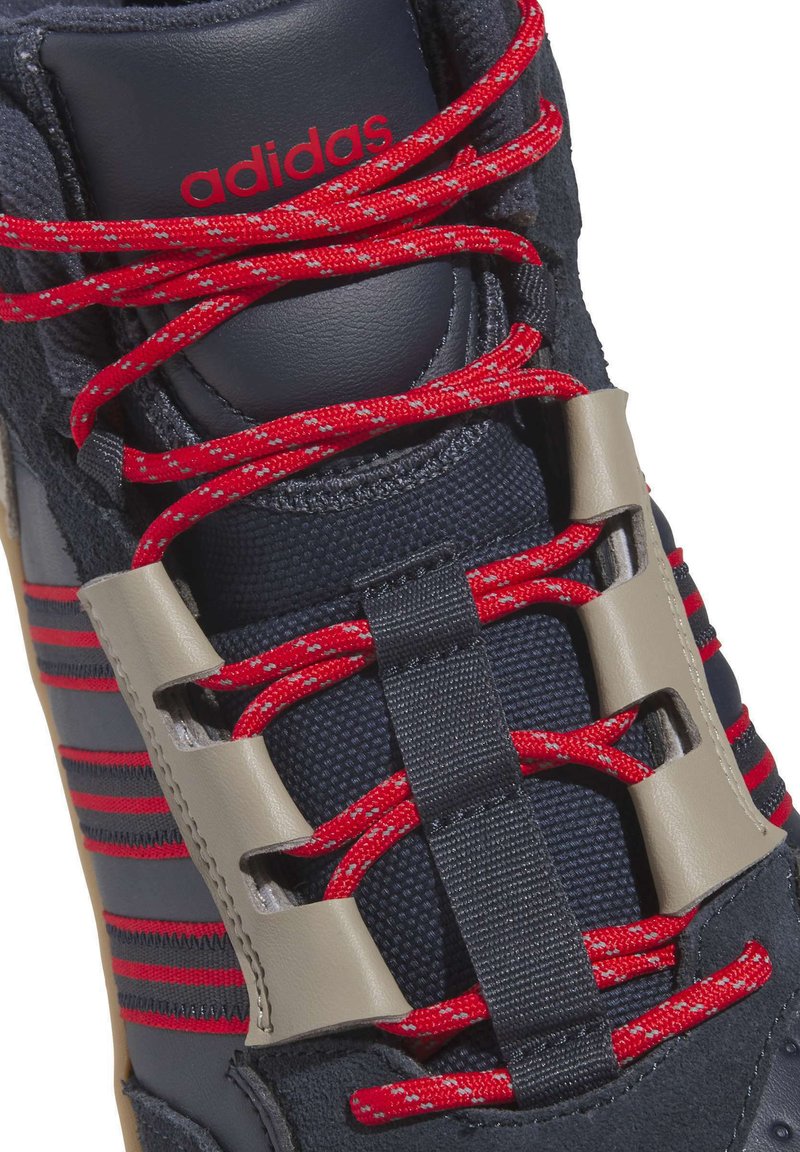 Marineblå sportssko med røde snørebånd, grå detaljer og tekstureret overdel. Har en polstret krave og synlig logo på tungen.