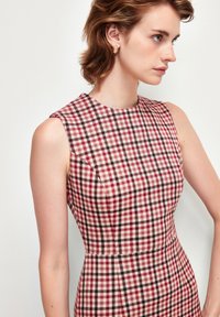 Löpare sleeveless-mekko punaisessa ja beige ruutukuosissa. Materiaali näyttää teksturoidulta ja sileältä. Pyöreä pääntie ja räätälöity siluetti.