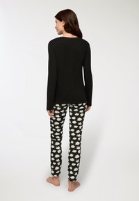 Maglietta nera a maniche lunghe abbinata a pantaloni neri a fantasia con disegni di nuvole bianche; tessuto morbido, stile aderente, dettagli minimi.