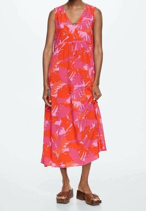 Robe sans manches à col en V avec imprimé de feuilles tropicales rouges et roses, longueur midi, portée avec des sandales compensées marron sur une personne debout.