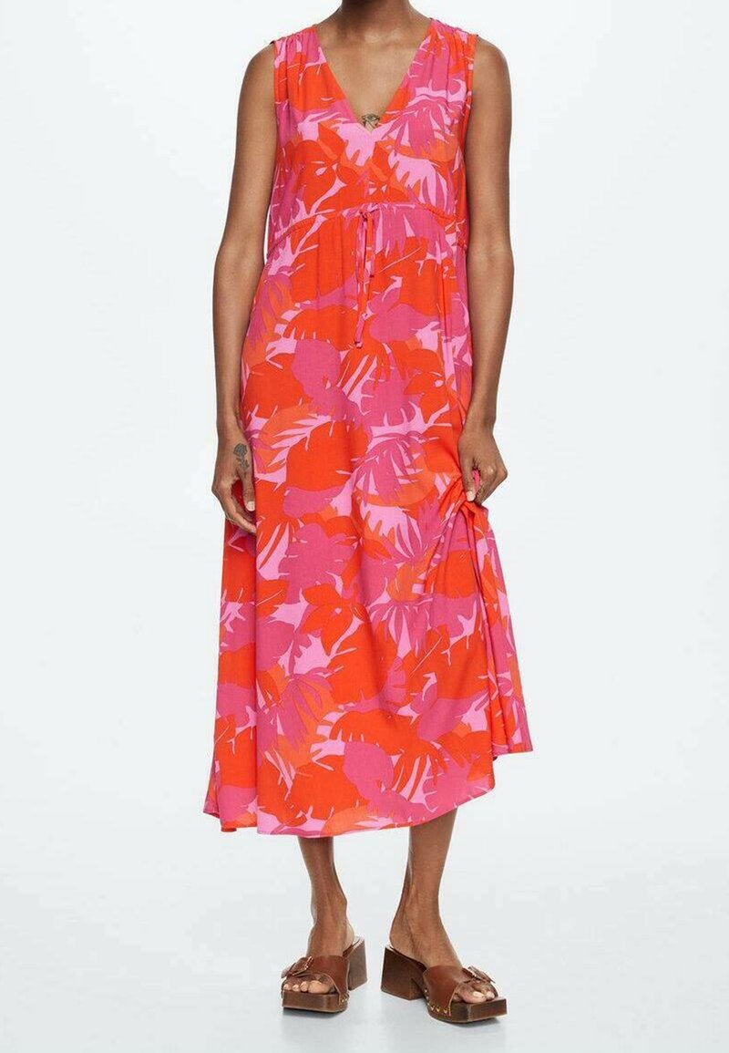 Robe sans manches à col en V avec imprimé de feuilles tropicales rouges et roses, longueur midi, portée avec des sandales compensées marron sur une personne debout.
