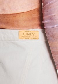 Valkoiset farkut, joissa on kultainen nahkalappu, jossa lukee "ONLY", ja vaaleanpunainen, teksturoitu pitkähihaisvaate osittain näkyvissä ylhäällä.