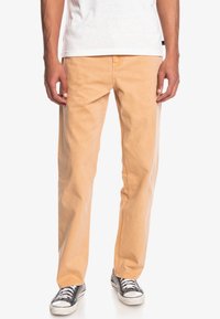 Chino chiari in cotone, con design a gamba dritta, tasche frontali e abbinati a sneaker nere e bianche.