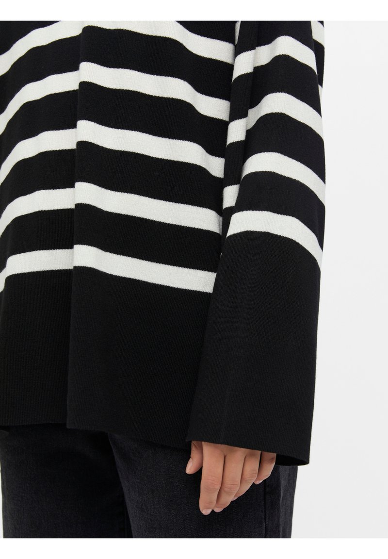 Pull rayé noir et blanc à manches longues, fabriqué en matière tricotée douce. Présente de larges rayures et un design à coupe ample.