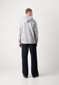 Lichtgrijze hoodie met een trekkoord capuchon, achternaad en geribde manchetten, gecombineerd met donkerblauwe wijde broek en zwarte schoeisel.