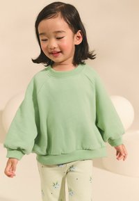 Sweat à col rond en polaire verte avec des manches surdimensionnées et des poignets côtelés, associé à un legging vert clair avec des motifs floraux bleus.