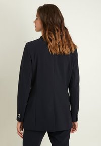 Blazer marine avec une coupe ajustée, un design à un seul bouton, des revers crantés et des accents à trois boutons sur les poignets.