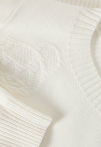 Suéter de punto blanco con un patrón texturizado, puños acanalados y un sutil diseño gráfico en relieve en el pecho. Tela suave.