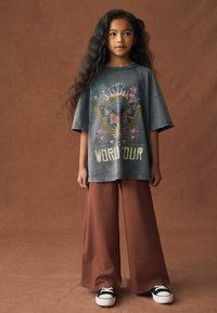 Grå oversized t-shirt med blomster- og sommerfuglegrafik, parret med brune ribbede bukser med vide ben og sorte sneakers med hvide snørebånd.