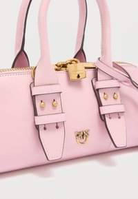 Ροζ δερμάτινη τσάντα χειρός με δύο χειρολαβές, χρυσές μεταλλικές λεπτομέρειες, λουκέτο και διακοσμητικές ραφές. Διαθέτει διακριτικό με το λογότυπο και διακοσμητικά καρφιά.