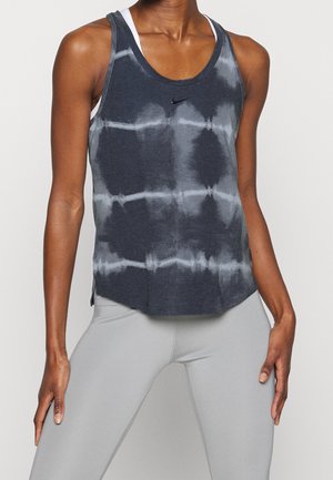 Femme portant un débardeur de sport noir et gris tie-dye par-dessus un soutien-gorge de sport blanc et un legging gris clair, debout les mains sur les hanches.