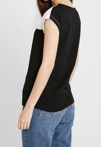 Czarny i biały krótki rękaw top z okrągłym dekoltem, wykonany z gładkiego materiału, z kontrastowym przeszyciem na rękawach.