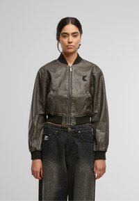 Tumedast nahast lühike bomber-jakk, millel on soonikvarrukad ja -äär, küljetaskud ning logoplaat rinnal.