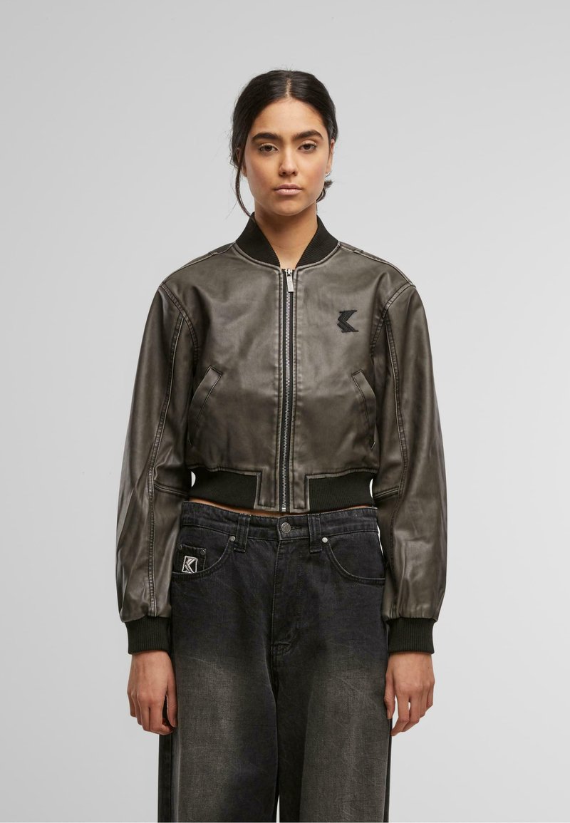 Tumedast nahast lühike bomber-jakk, millel on soonikvarrukad ja -äär, küljetaskud ning logoplaat rinnal.