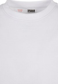 T-shirt en coton blanc avec un col rond, portant une étiquette "URBAN CLASSICS" et un label d'avertissement. Texture lisse et design simple.