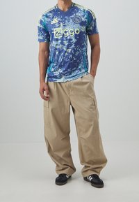 Niebieska i turkusowa wzorzysta koszulka z krótkim rękawem, z żółtym napisem "Ziggo" i trzema paskami na ramionach. Beżowe spodnie typu cargo, czarne sneakersy.