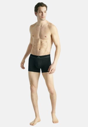 Schwarze Boxer Shorts aus dehnbarem Material, mit einem weichen Bund und Logo. Das Modell zeigt ein eng anliegendes Design und eine Länge bis zur Mitte des Oberschenkels.