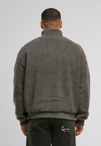 Grå fleece genser med høy krage og ribbestrikkede mansjetter, med en teksturert, fluffy overflate og en avslappet passform.