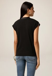Top nero a maniche corte con vestibilità rilassata, scollatura rotonda e polsini arrotolati. Il tessuto appare liscio e leggero.