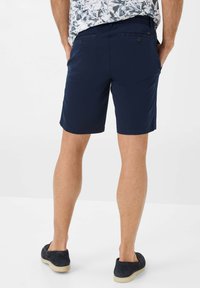 Pantaloni corti blu navy realizzati in un tessuto dalla trama liscia. Presentano due tasche posteriori con bottoni e un taglio semplice e dritto.